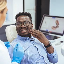 Smiling man in a dental chair touching his cheek